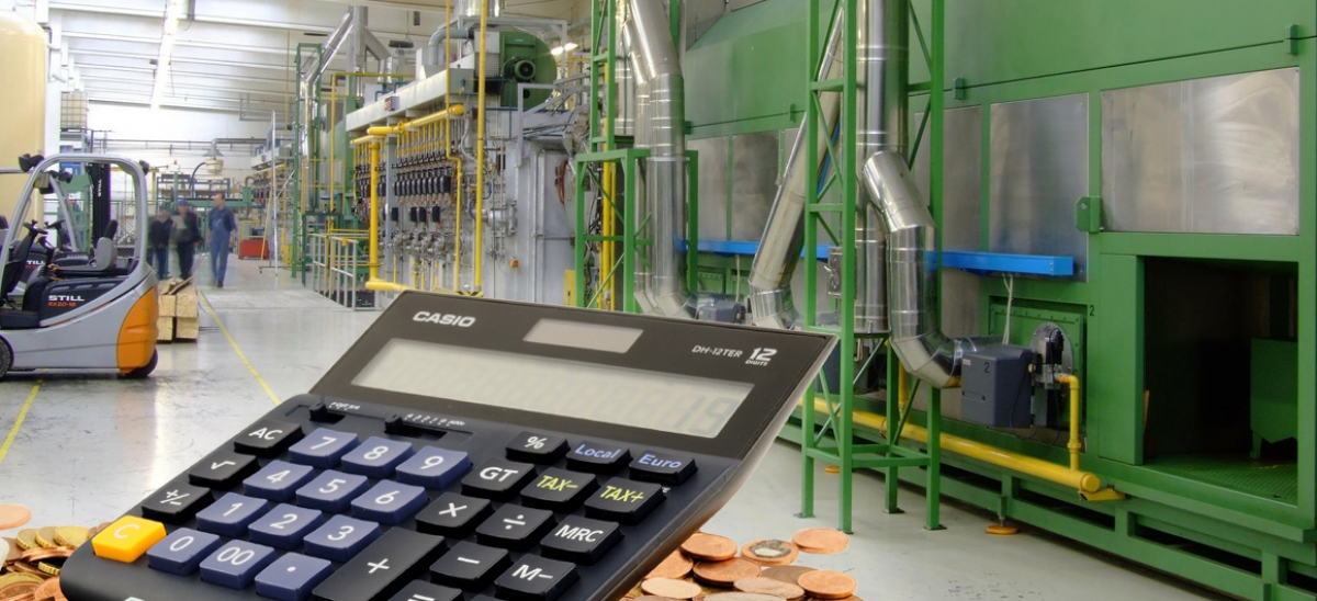 Ein Taschenrechner und Geld vor dem Innenraum einer Industrieanlage (Symbolbild)